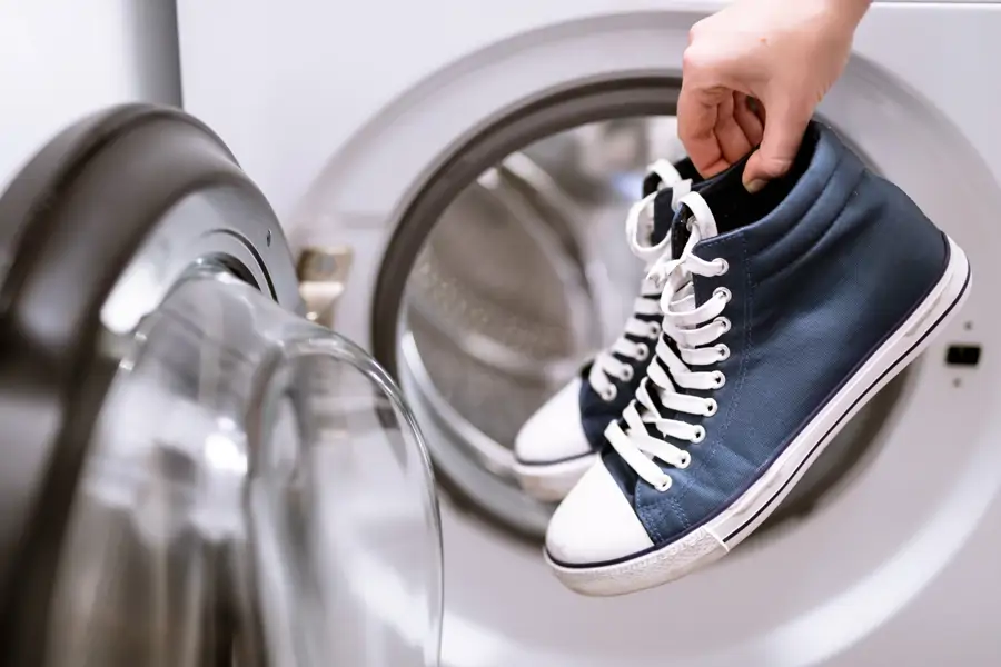Mujer sosteniendo unas zapatillas junto a una lavadora